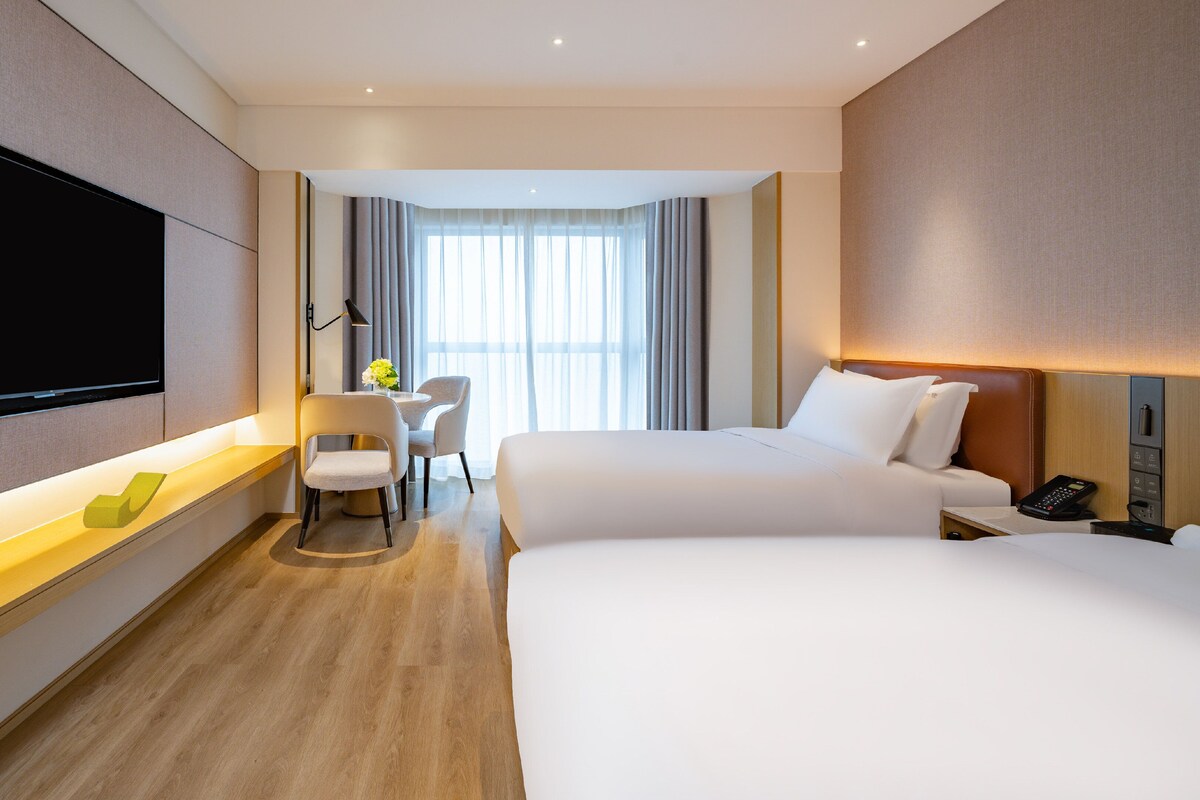 Habitación de hotel con una cama grande, un escritorio con silla, televisión montada en la pared y una ventana con cortinas.