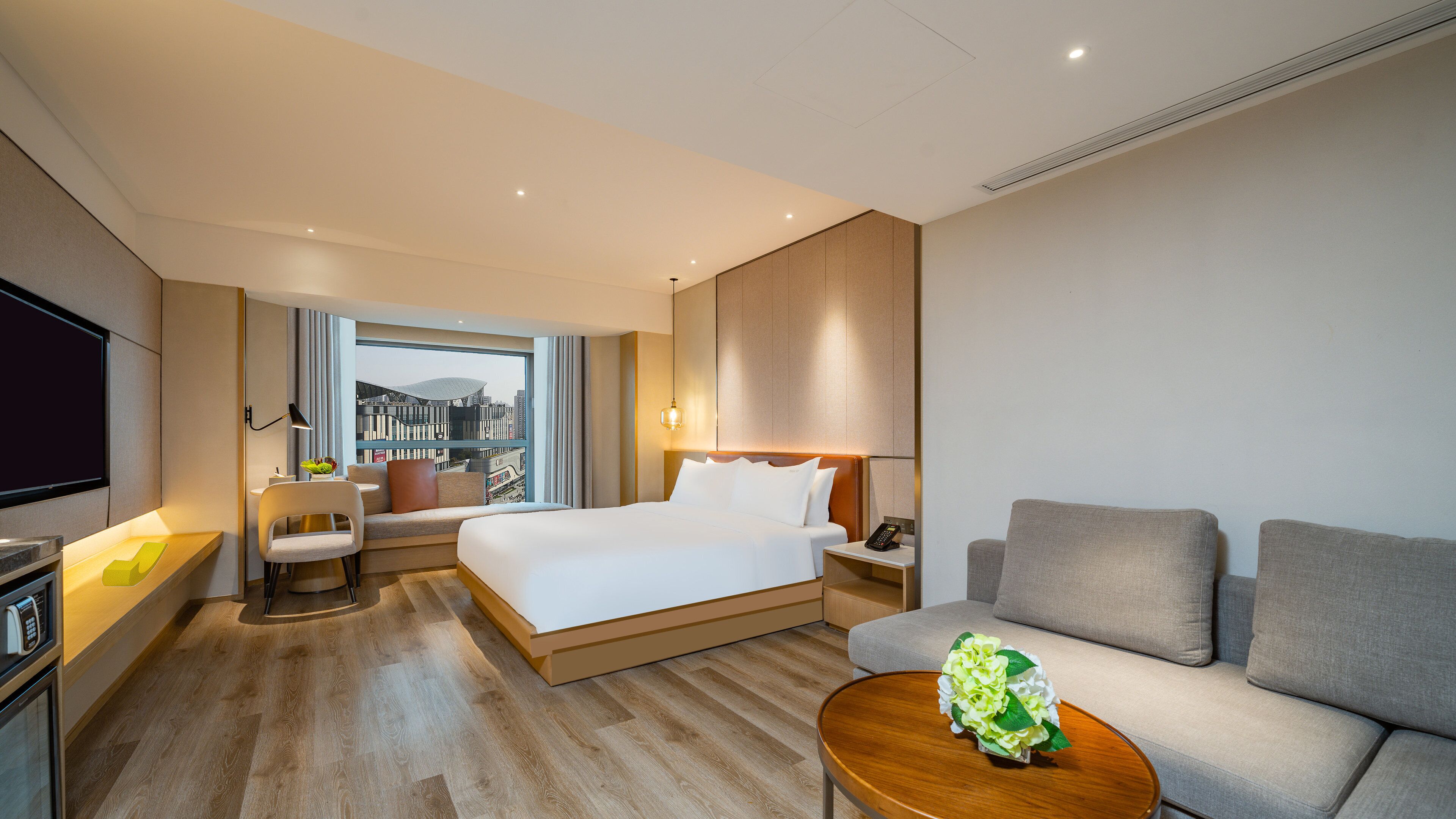 Ein Hotelzimmer mit einem Bett, einem Sofa, einem Couchtisch, einem Fernseher und Blick auf eine Stadtansicht.