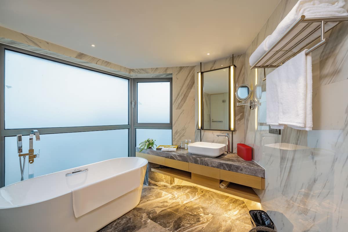 A modern bathroom with a large bathtub, a vanity with a sink, a mirror, and a window providing a view.
