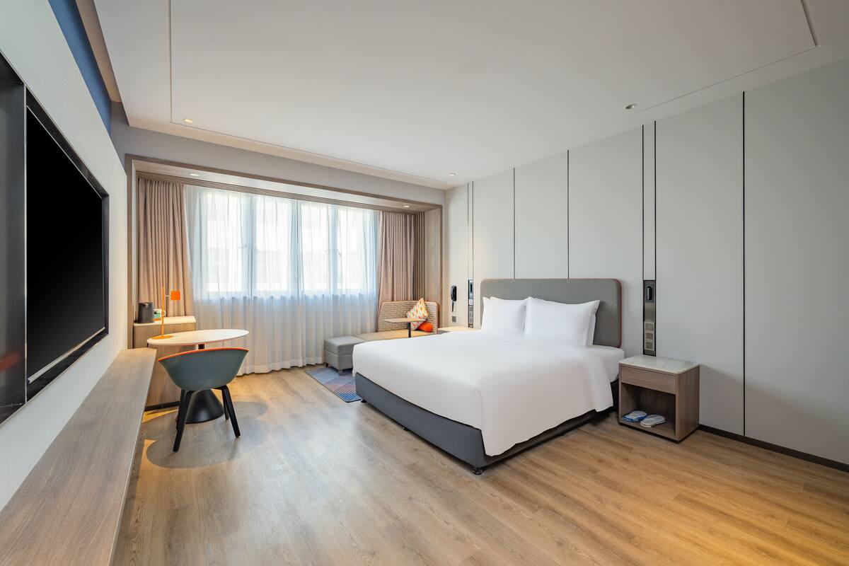 A modern hotel room with a large bed, a desk, and a TV.