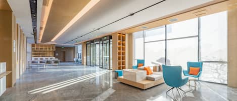 A spacious lobby with a marble floor, modern seating, and large windows offering a view of the outdoors.