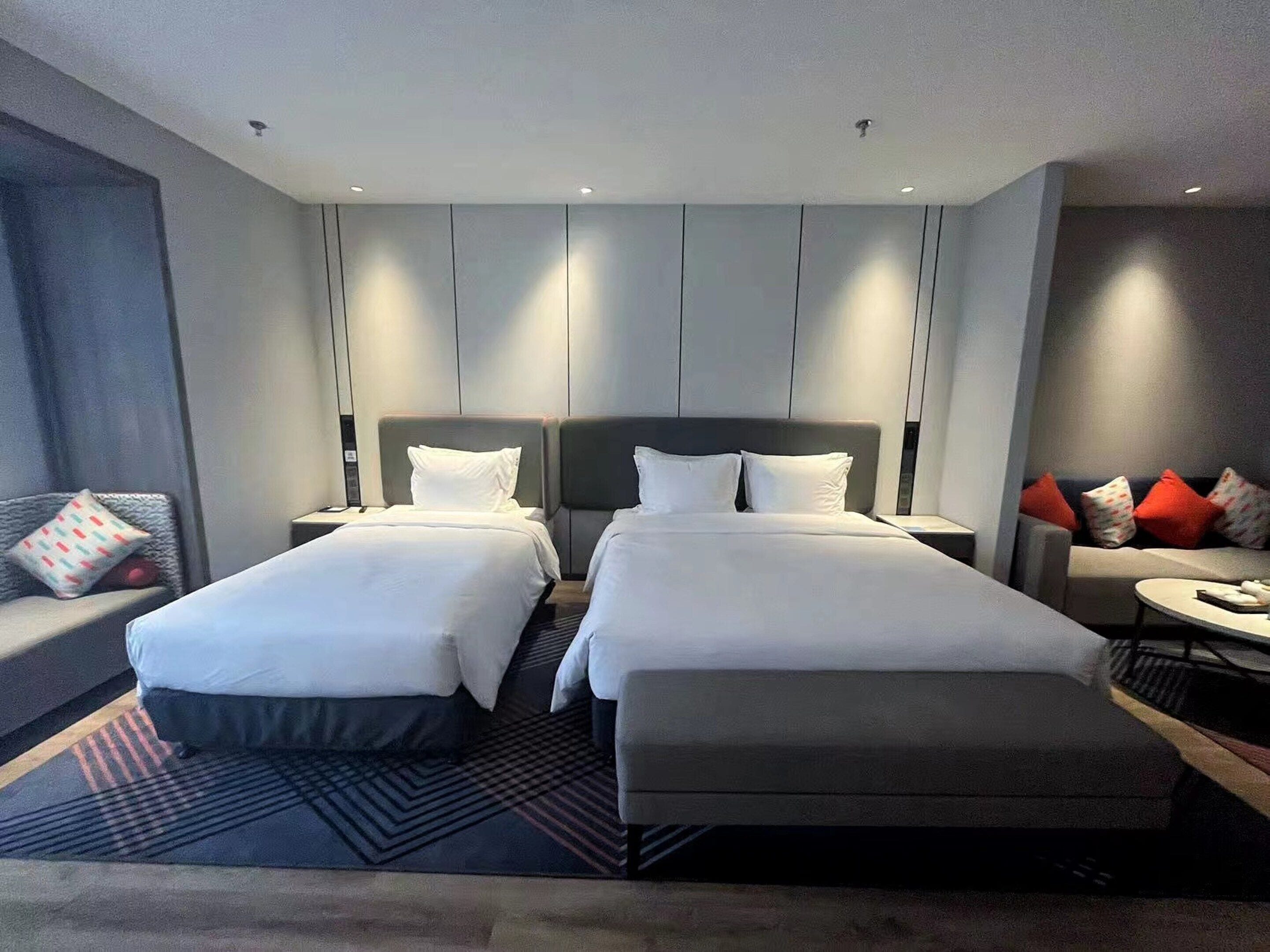 Ein modernes Hotelzimmer mit zwei Betten, einem Sofa und einem kleinen Tisch.