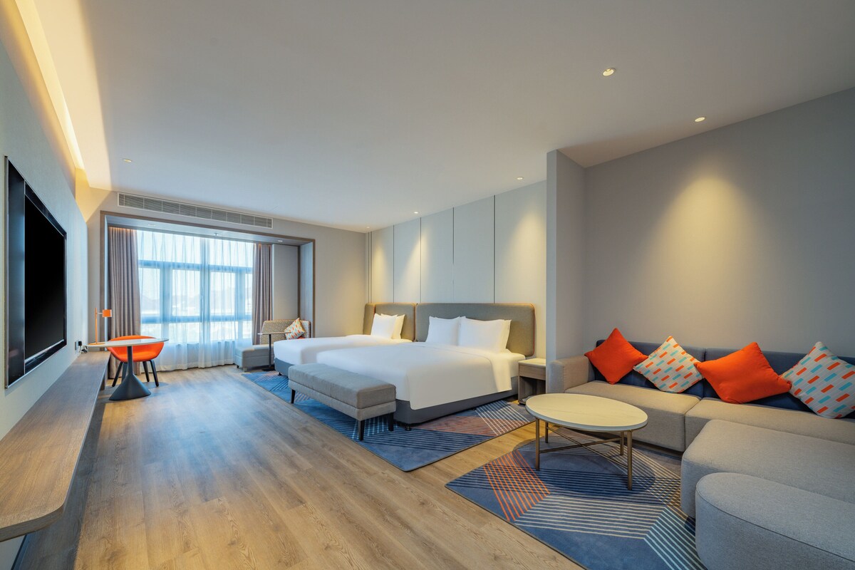 A modern hotel room with a large bed, a sofa, a TV, and a desk.