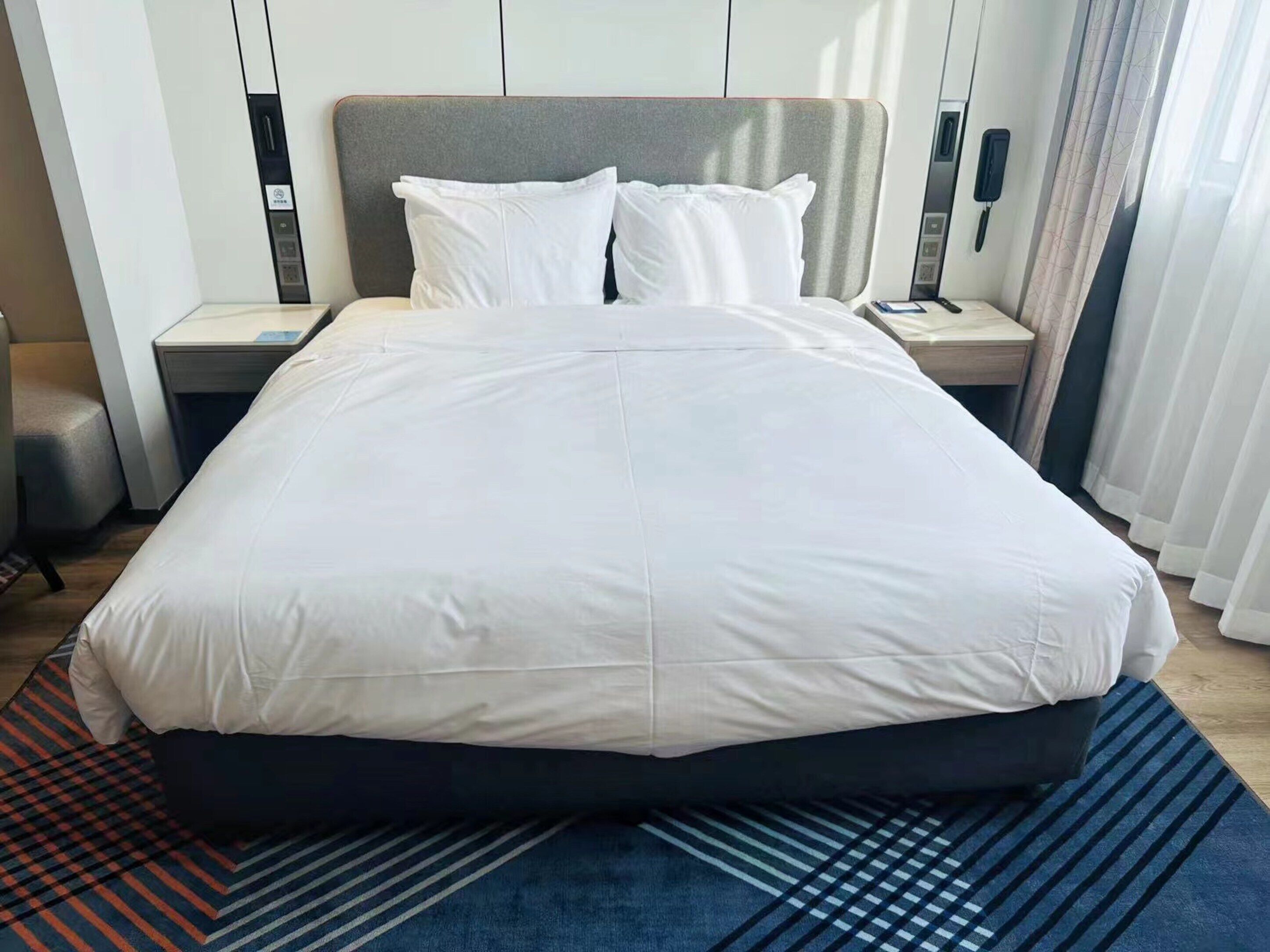 Een hotelkamer met een groot bed, een nachtkastje, een telefoon en een raam met gordijnen.