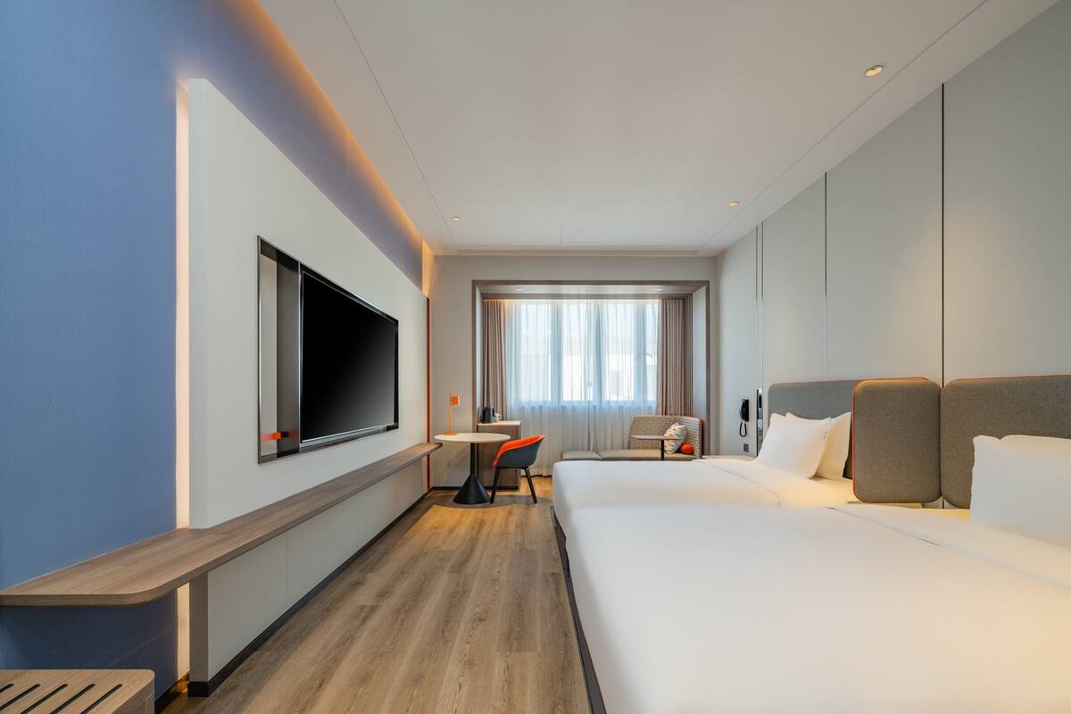 A hotel room with a large bed, a desk, a TV, and a window with curtains.