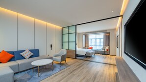 A modern hotel room with a sofa, armchair, and a small table. There is a large window with curtains and a flat-screen TV mounted on the wall. - Holiday Inn Express Suzhou Luzhi by IHG (Suzhou)