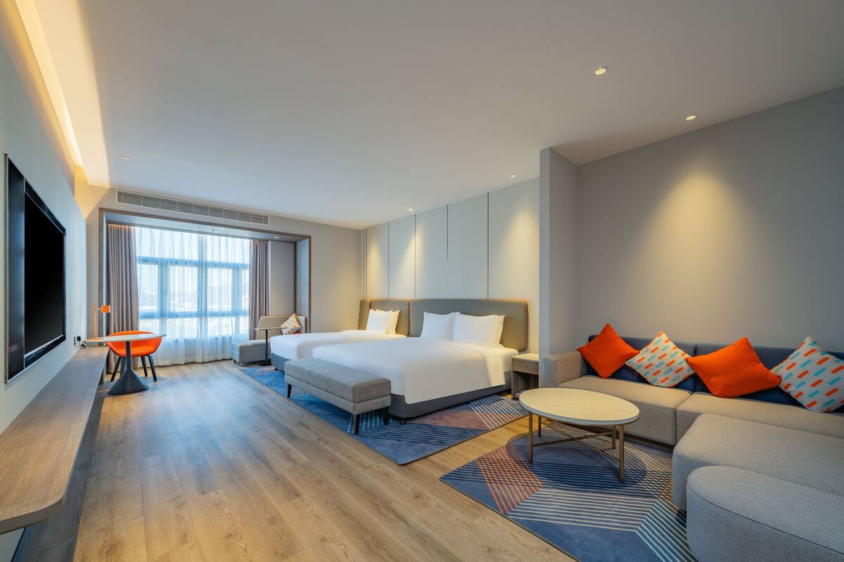 A modern hotel room with a large bed, a sofa, a TV, and a desk.