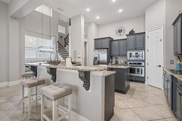 A modern kitchen with a central island, grey cabinets, stainless steel appliances, and a staircase leading to another level.