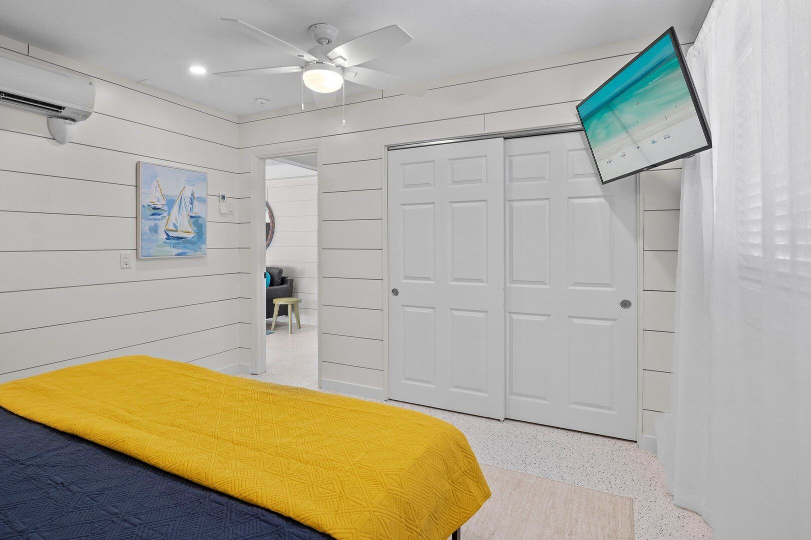 Une chambre à coucher avec un lit, un ventilateur de plafond, une télévision et une porte.