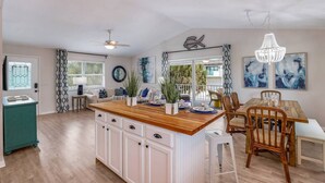 A spacious kitchen with a wooden island, white cabinetry, and a dining area with wooden chairs and a table. - On Point: Across Street from Bean Point Beach, Outdoor Games & Pool by Anna Maria Life (Anna Maria)