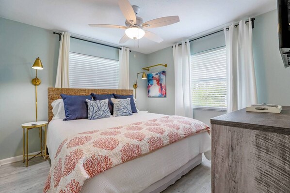 A bedroom with a bed, a ceiling fan, a nightstand, a lamp, and a painting. - On Point: Across Street from Bean Point Beach, Outdoor Games & Pool by Anna Maria Life (Anna Maria)