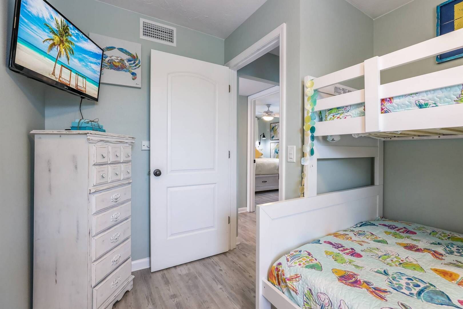 A bedroom with a bunk bed, a dresser, a television, and a door leading to another room.