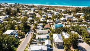 An aerial view of a coastal residential area with houses, a beach, and clear blue waters. - On Point: Across Street from Bean Point Beach, Outdoor Games & Pool by Anna Maria Life (Anna Maria)