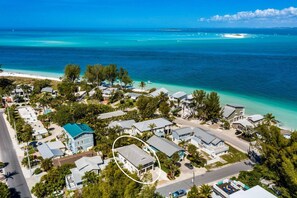 Ett flygbildsbild av ett bostadsområde vid kusten med hus, en strand och klart, blått vatten.