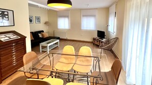 Una sala de estar moderna con una mesa de comedor de vidrio, sillas amarillas, un sofá negro, una mesa de centro blanca y una lámpara colgante negra.