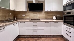 Una cocina moderna con gabinetes blancos, encimeras de granito, electrodomésticos de acero inoxidable y un televisor integrado.