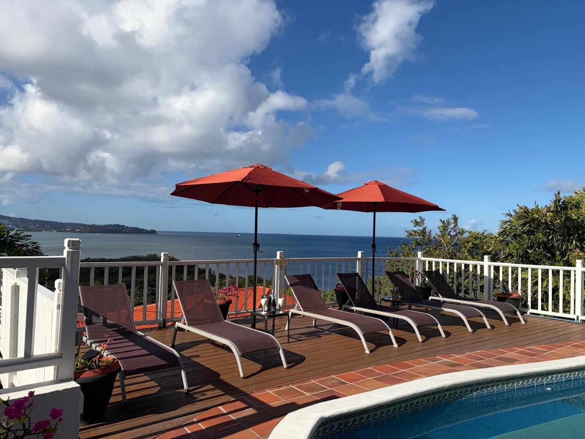 Área de piscina com espreguiçadeiras e guarda-sóis vermelhos, com vista para um corpo de água.