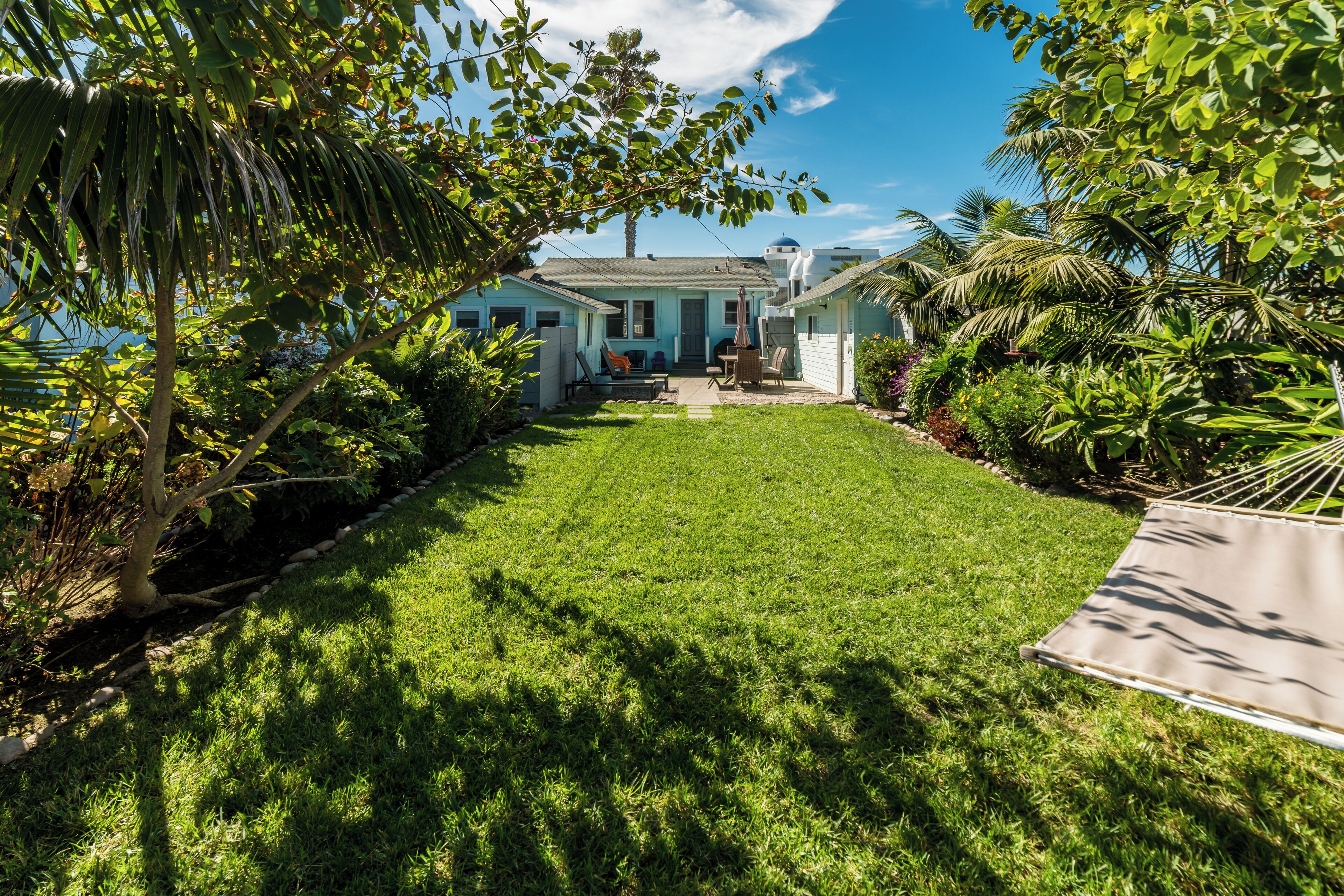 A residential property with a well-maintained lawn, a hammock, and a variety of tropical plants.