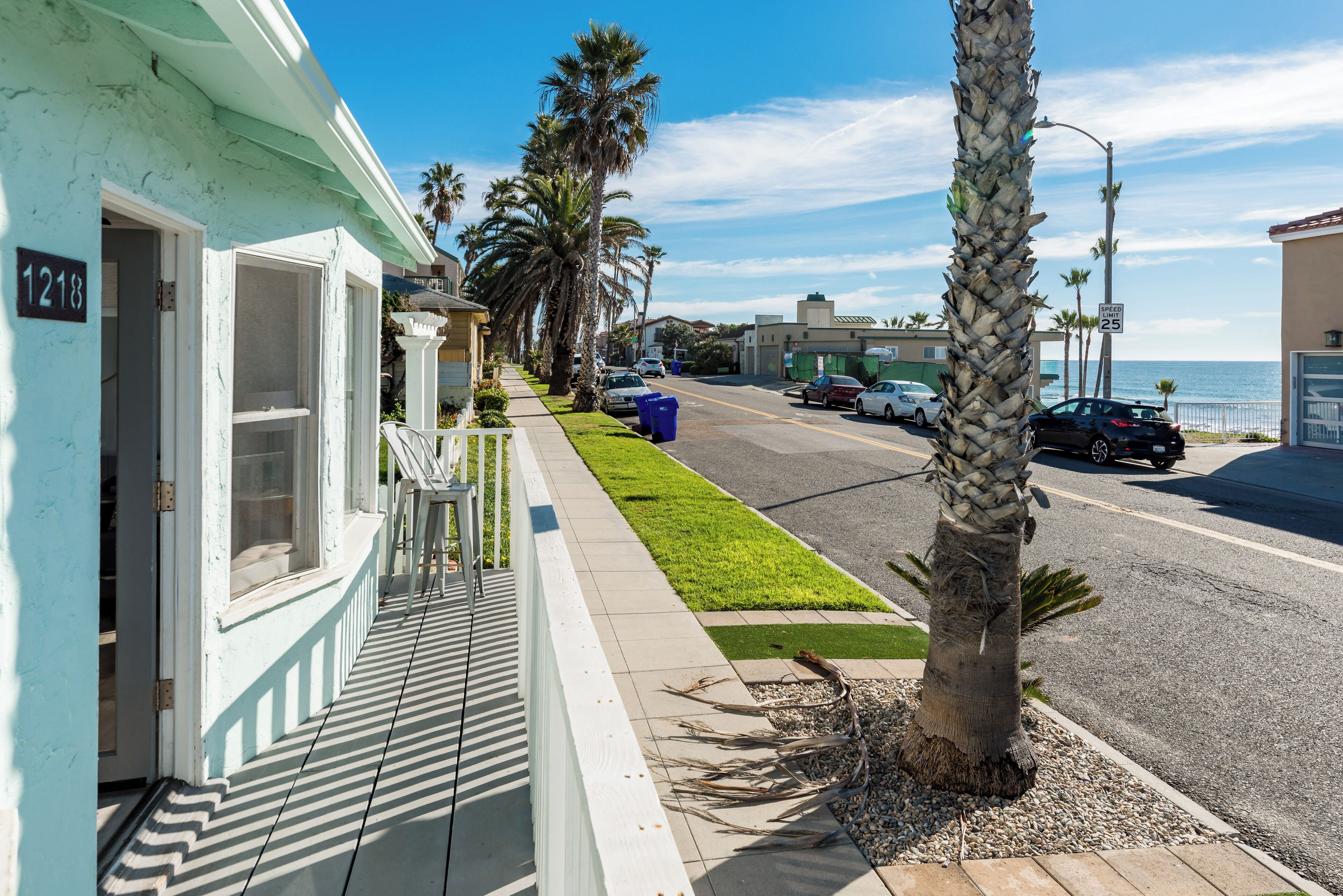 A coastal building with a numbered door, a sidewalk, parked cars, and palm trees.