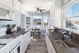 A modern kitchen with white cabinets, a gas stove, a sink, and a dining area with a table and chairs.