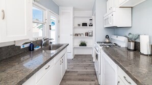 A modern kitchen with white cabinets, granite countertops, and a built-in stove. - Pacific Bungalow (Oceanside)