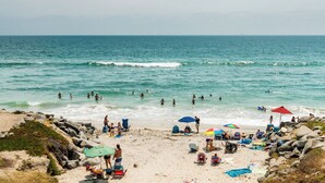A beach with people swimming and sunbathing, umbrellas, and beach chairs. - Pacific Bungalow (Oceanside)