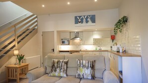 A modern living room with a sofa, a staircase, and a kitchen area. - Cringol Cottage (Ambleside)