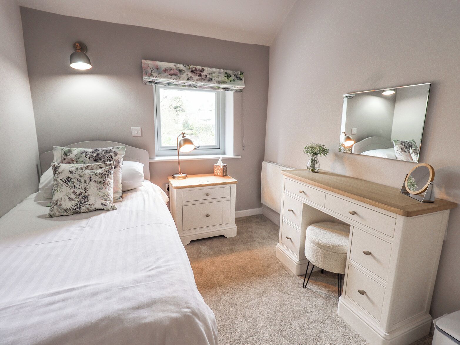 A bedroom with a bed, a desk, a chair, a window with a view, and a mirror.