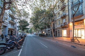 A tree-lined street with parked motorcycles and a building with a sign reading "Albert La-Kosa".