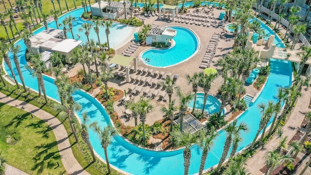 Eine Vogelperspektive auf ein Resort mit mehreren Schwimmbecken, Liegestühlen und Palmen.