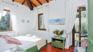 Une chambre à coucher avec un lit, une table de chevet verte, une fenêtre avec des rideaux, un tableau et une vue sur les arbres.