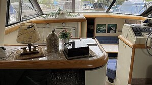 Interior de un barco con mostrador de madera, lámpara, jarrón decorativo y panel de control.