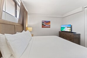 Een hotelkamer met een groot bed, een televisie op een houten dressoir, een schilderij aan de muur en een raam met gordijnen.