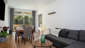 A living room with a grey sofa, a dining table with chairs, a TV mounted on the wall, and a window with curtains. - Sagrada Familia bright apartment with balcony (08013 Barcelona)
