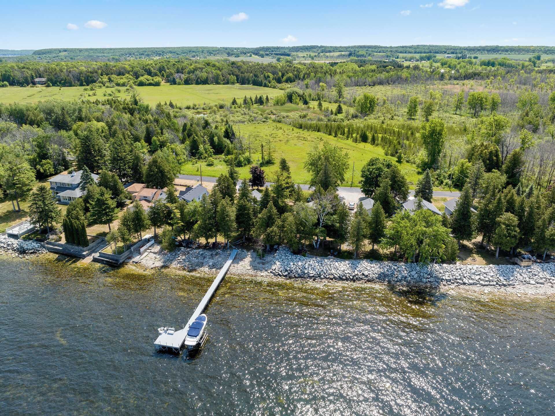 An aerial view of a lakeside property with a dock, houses, and surrounding greenery.
