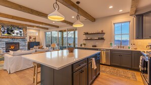 Una cocina moderna con una isla grande, vigas de madera, una chimenea y vistas al exterior.