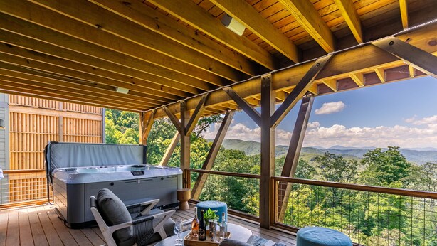 Una terraza de madera con un jacuzzi, asientos y una mesa con una botella y vasos.