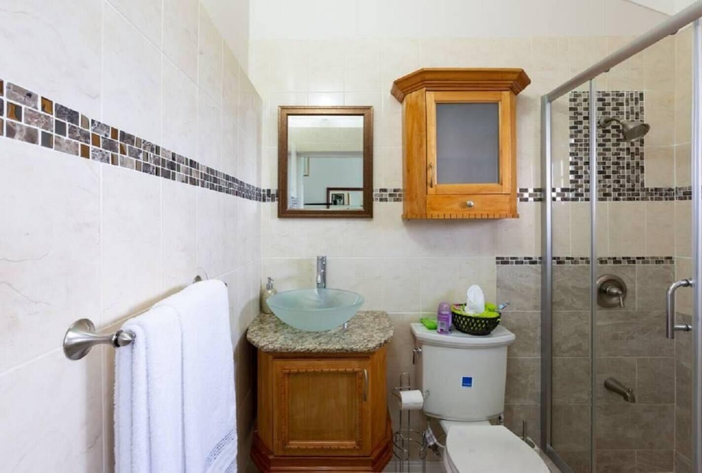 Une salle de bain avec un lavabo en verre, un meuble en bois, des toilettes et un espace douche.