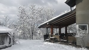 A covered outdoor area with a patio, a stone wall, and snow-covered trees. - Dominating Olywood One (Sarajevo)