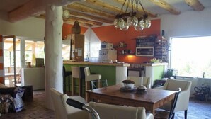 A dining area with a wooden table and chairs, a kitchen in the background, and a window with a view. - Dominating Olywood One (Sarajevo)