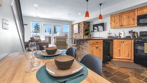 A modern kitchen with wooden cabinets, a stone backsplash, and a dining area with a table set for two.