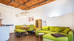 Een moderne woonruimte met een houten plafond, een groene bank, een eettafel met stoelen, een klein wit tafeltje en een kast.