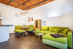 Un espace de vie moderne avec un plafond en bois, un canapé vert, une table à manger avec des chaises, une petite table blanche et un meuble.