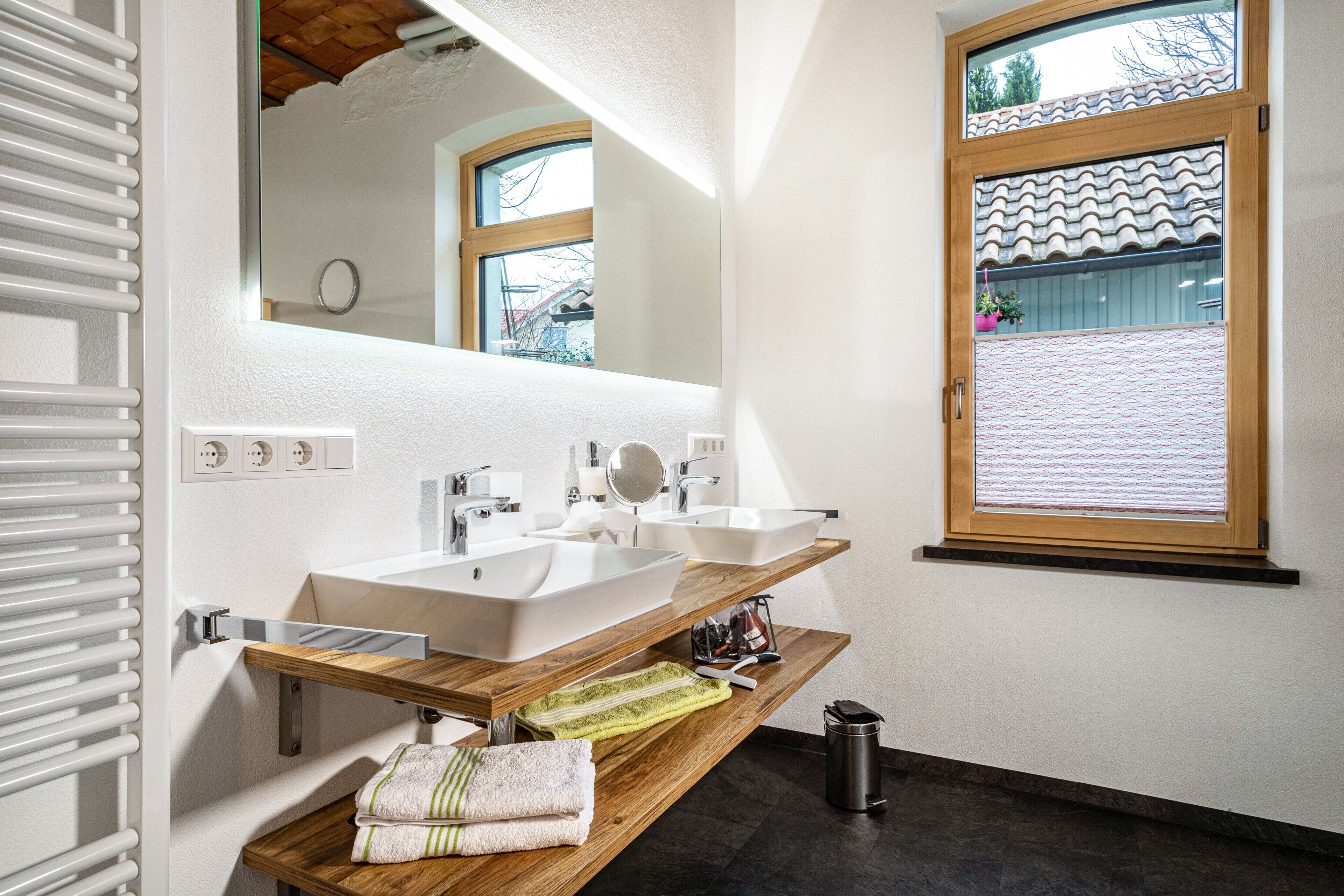 Une salle de bain moderne avec deux lavabos, un miroir, une fenêtre donnant sur un beau paysage et un porte-serviettes.