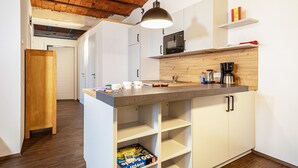 Een moderne keuken met een centraal eiland, witte kasten, een houten aanrechtblad en een bakstenen plafond.