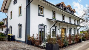 Een gebouw met twee verdiepingen, een witte gevel, meerdere ramen en een gele deur.