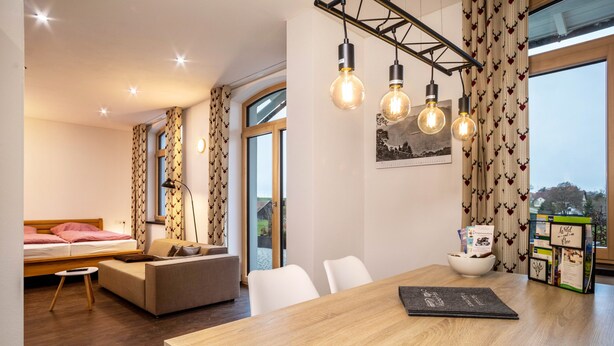 Een moderne kamer met een houten eettafel, een bank, een bed en uitzicht op de omgeving.