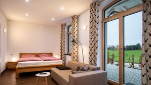 Een slaapkamer met een bed, een bank, een klein tafeltje en een groot raam met gordijnen.