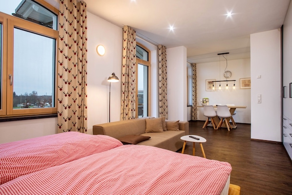 A hotel room with two beds, a sofa, a small table, and a dining area with chairs.