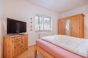 Une chambre à coucher comprenant un lit, une armoire en bois, un téléviseur posé sur un meuble en bois, et une fenêtre donnant sur des arbres.